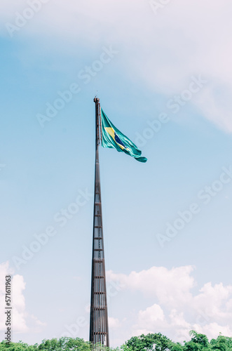 Brazilian flag flying, fluttering in the wind and with the blue sky in the background.