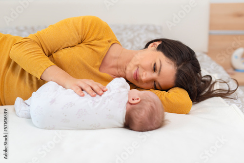 Mother and child on a white bed. Mom and baby boy in diaper playing in sunny bedroom. Parent and little kid relaxing at home