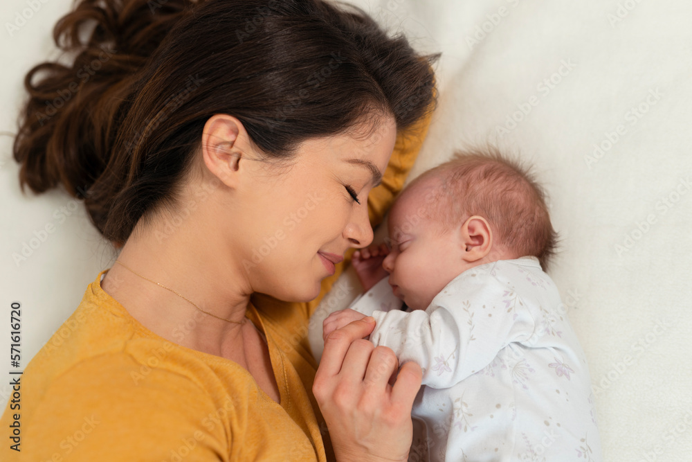 Mother and child on a white bed. Mom and baby boy in diaper playing in sunny bedroom. Parent and little kid relaxing at home