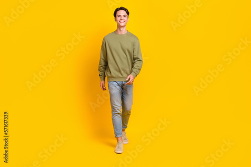 Full body photo of satisfied positive man toothy smile walking empty space isolated on yellow color background
