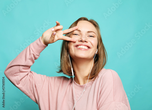 charming smiling young woman dressed pink sweater and show v-sign over blue background