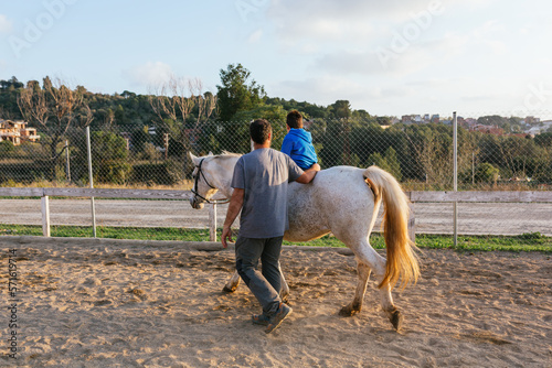 Child with disabilities riding a horse in an equine therapy session with an instructor. © Jordi Mora