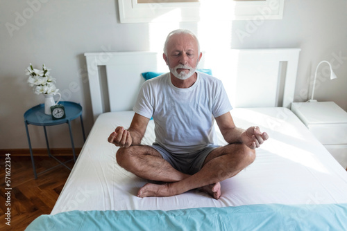 Indoor shot of senior man sitting peacefully on bed at home with his eyes closed. Mature man sitting on a bed and doing meditation.