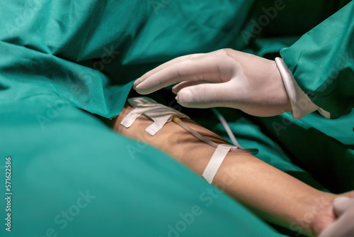 surgeon group tape tube patient arm for infusion therapy. team of surgery staff putting tape glue sodium tube to person. professional surgeon stick sodium chloride saline iv bag cord on patient arm
