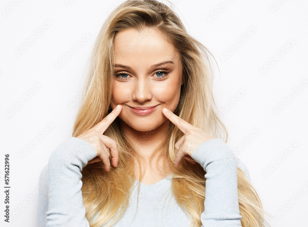 A cheerful funny young woman grimaces at the camera, presses her fingers to her cheeks, having fun. Lifestyle and emotion concept. A cheerful funny young woman grimaces at the camera, presses her fingers to her cheeks, having fun. Lifestyle and emotion concept.