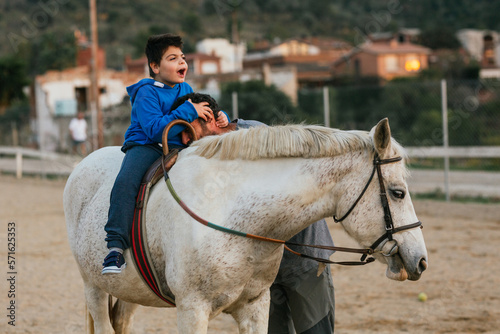 Boy with disabilities on the horse holding on to his equine therapy instructor.