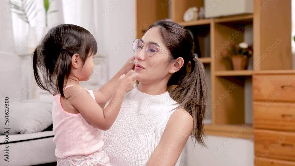 4K, Beautiful daughter sits on mother's lap, naughty daughter playing with clear scotch tape, trying put it on mom's face, mother sits lets daughter play looks at daughter happily. 4K, Beautiful daughter sits on mother's lap, naughty daughter playing with clear scotch tape, trying put it on mom's face, mother sits lets daughter play looks at daughter happily.