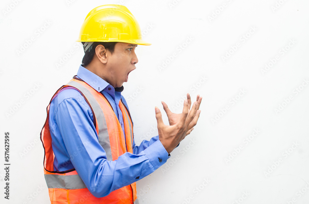side view of stressed over work concept illustrated by asian male construction worker in blue shirt, orange vest and yellow safety helmet with furious, mad, sad, angry expression. overworked concept side view of stressed over work concept illustrated by asian male construction worker in blue shirt, orange vest and yellow safety helmet with furious, mad, sad, angry expression. overworked concept