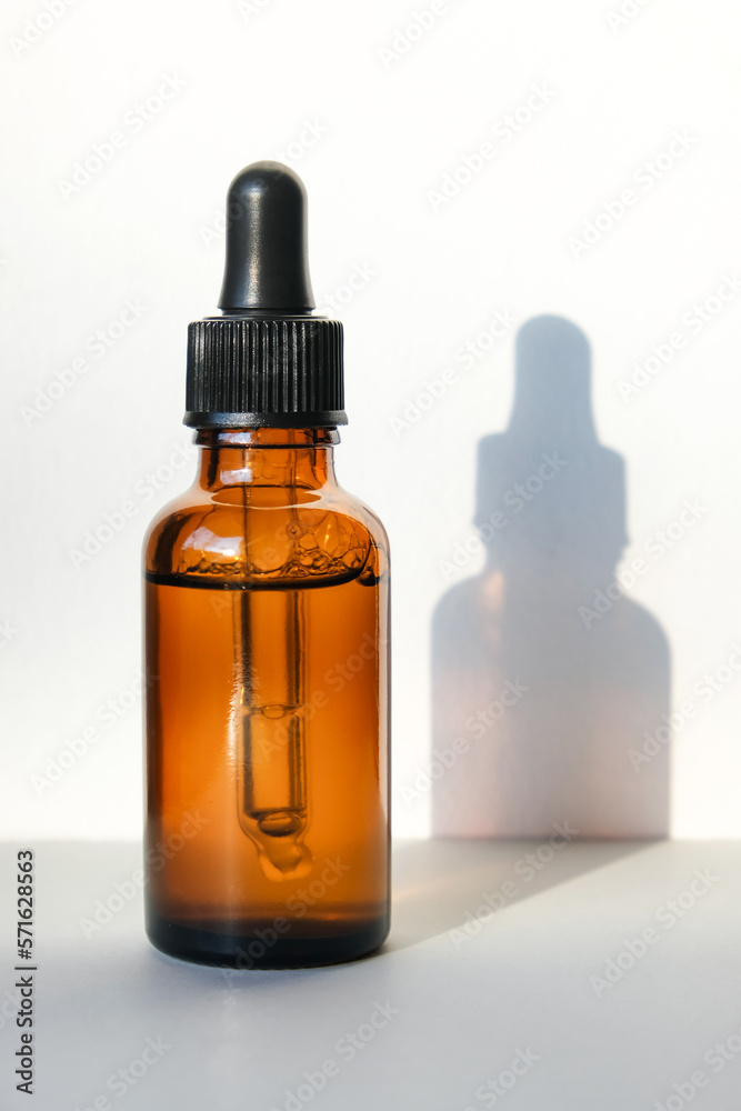 Amber pipette bottle casts a shadow on a gray background. Vertical image, flat lay, copy space.