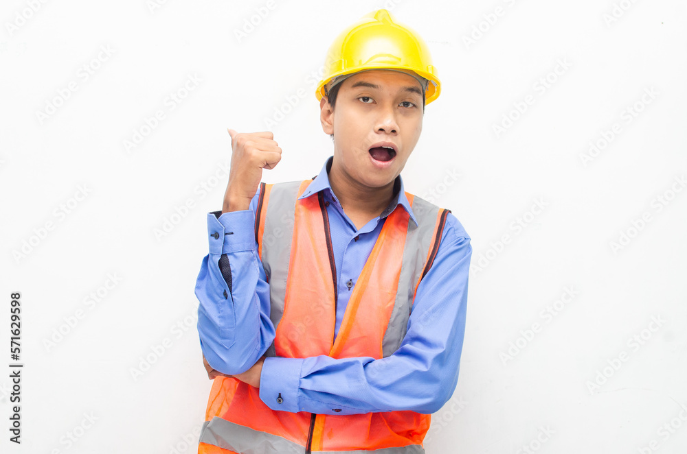 asian construction worker wearing yellow safety helmet and vest smiling and pointing finger with happy and shocked expression. billboard model advertisment concept. 
