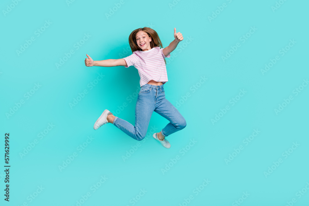 Full length photo of charming pretty girl dressed pink t-shirt jumping high showing thumbs up isolated teal color background