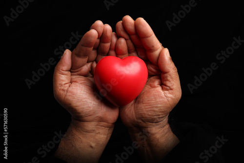Asian dark skin top view two hand holding making red hart love shape sign on black background