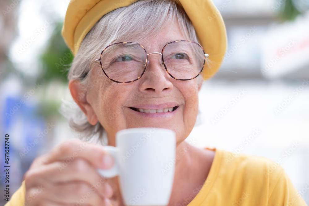 Closeup portrait of smiling attractive elderly woman in yellow enjoying an espresso coffee cup. Elderly caucasian lady relaxed in outdoor coffee shop Closeup portrait of smiling attractive elderly woman in yellow enjoying an espresso coffee cup. Elderly caucasian lady relaxed in outdoor coffee shop