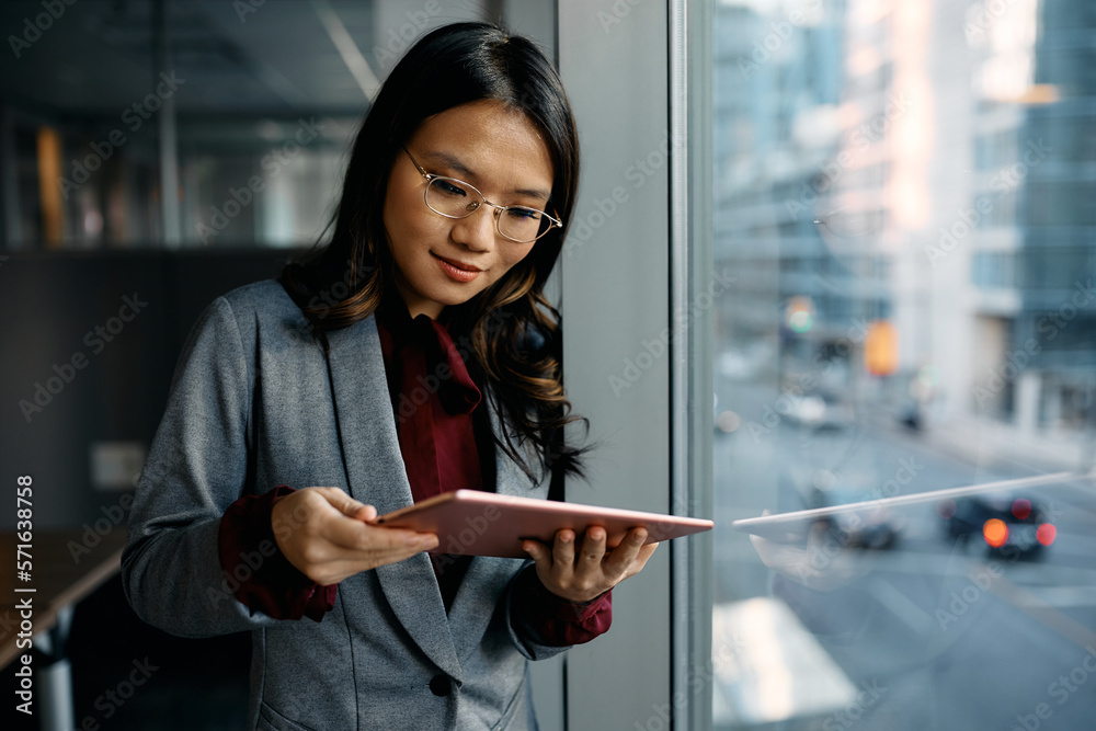© Drazen - Asian female executive using digital tablet by window.