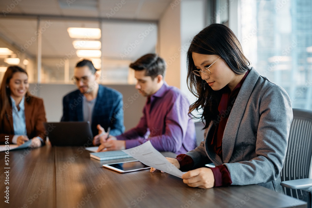 Fototapeta premium Asian businesswoman reads documents during meeting with coworkers in office.