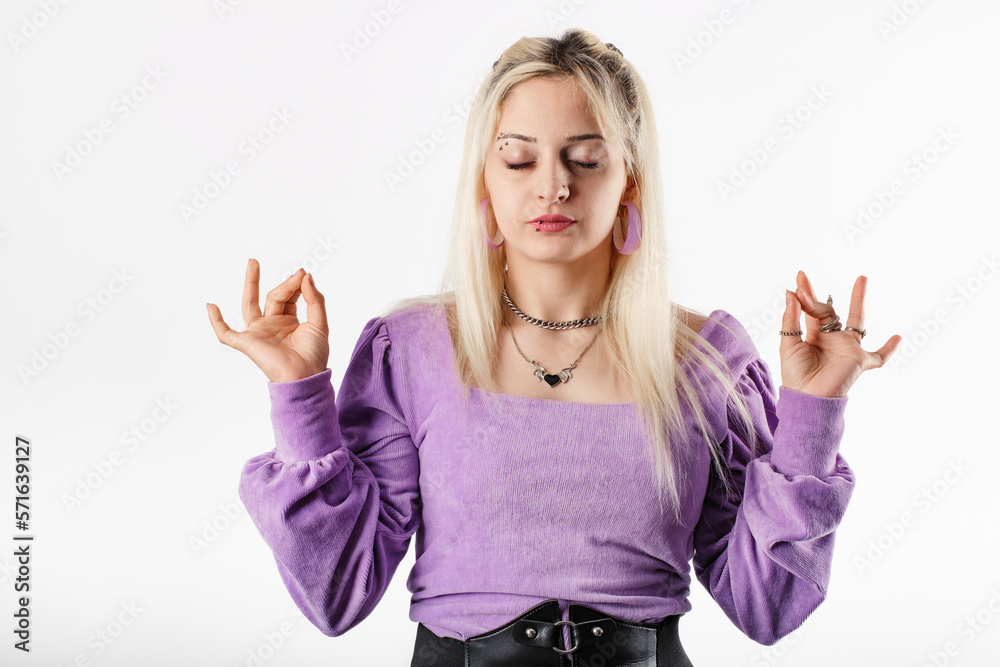 Woman standing isolated over white background keeping eyes closed, holding fingers in mudra gesture. Meditation, religion and spiritual practices. Peace and calm. Releases all tension and stress. Woman standing isolated over white background keeping eyes closed, holding fingers in mudra gesture. Meditation, religion and spiritual practices. Peace and calm. Releases all tension and stress.