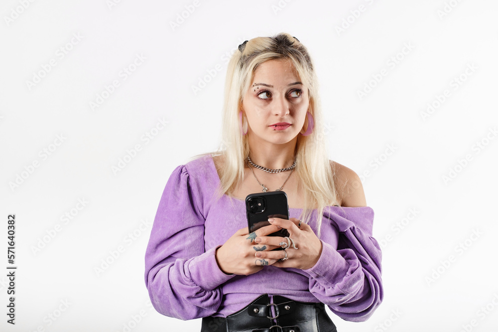 Portrait of young blonde woman isolated over white background smiles, looks at the empty copy space while holding the phone at chest level. Looking an advertisement or a campaign or a discount. Portrait of young blonde woman isolated over white background smiles, looks at the empty copy space while holding the phone at chest level. Looking an advertisement or a campaign or a discount.