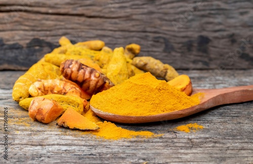 Closeup of Raw Turmeric Root and Turmeric Powder in a Wooden Ladle Isolated on Wooden Background © Arnav