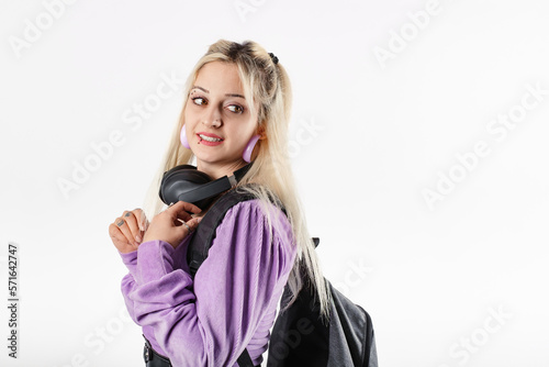 Side view of cheerful woman wearing blouse standing isolated over white background with headphones and backpack. Education school university college concept. Looks back.
