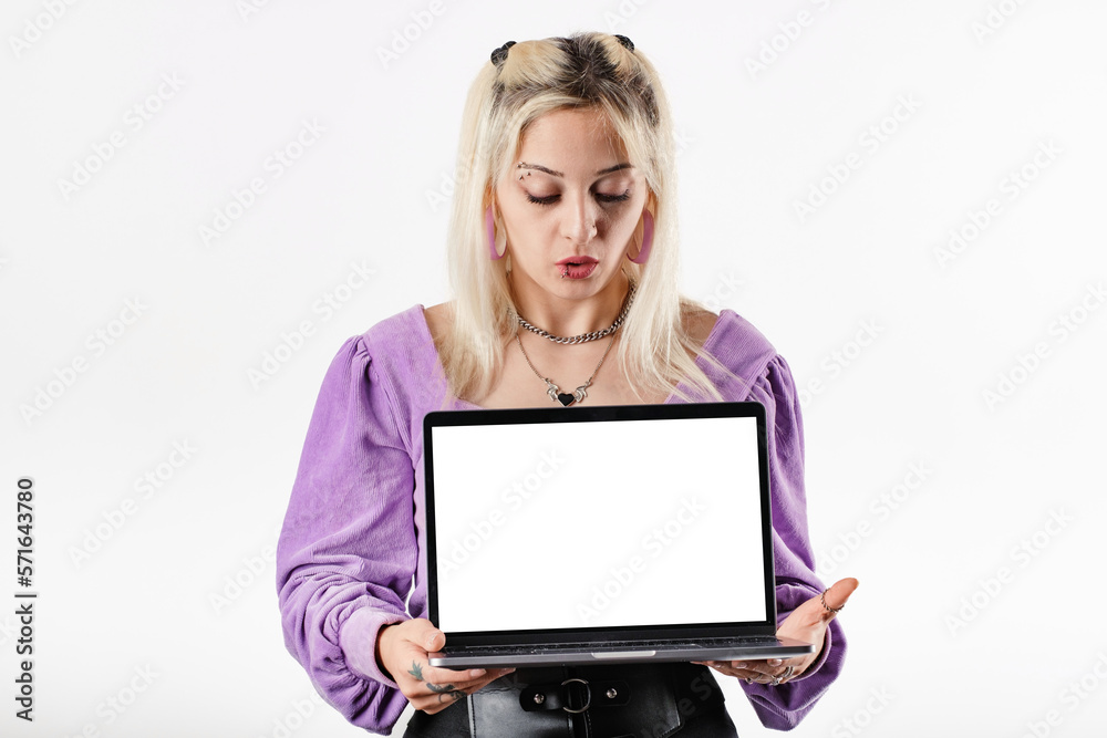 Beautiful blonde woman wearing ribbed blouse standing isolated over white background holding a laptop with a blank white screen stares at the screen of computer with a confused, excited expression. Beautiful blonde woman wearing ribbed blouse standing isolated over white background holding a laptop with a blank white screen stares at the screen of computer with a confused, excited expression.