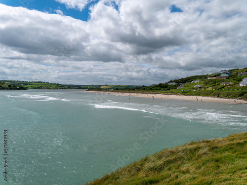 View of Inchydoney beach from the Cape of the Virgin Mary. Irish seascape. A European settlement on the shore. Green grass near body of water under cloudy sky