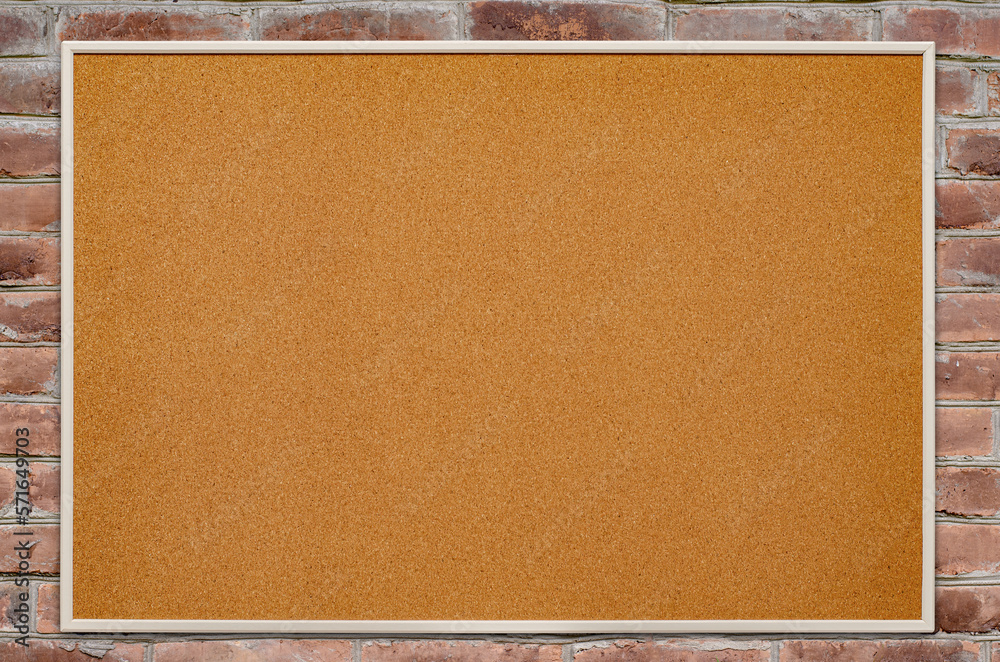 Fototapeta premium An empty cork board is hanging on a brick wall. Copy space.