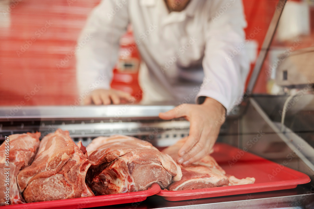 A meat shop worker is reaching for fresh raw meat and selling it.