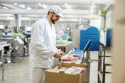 Fotografía A meat processing plant worker is packing ground meat into the boxes while standing next to a conveyor belt