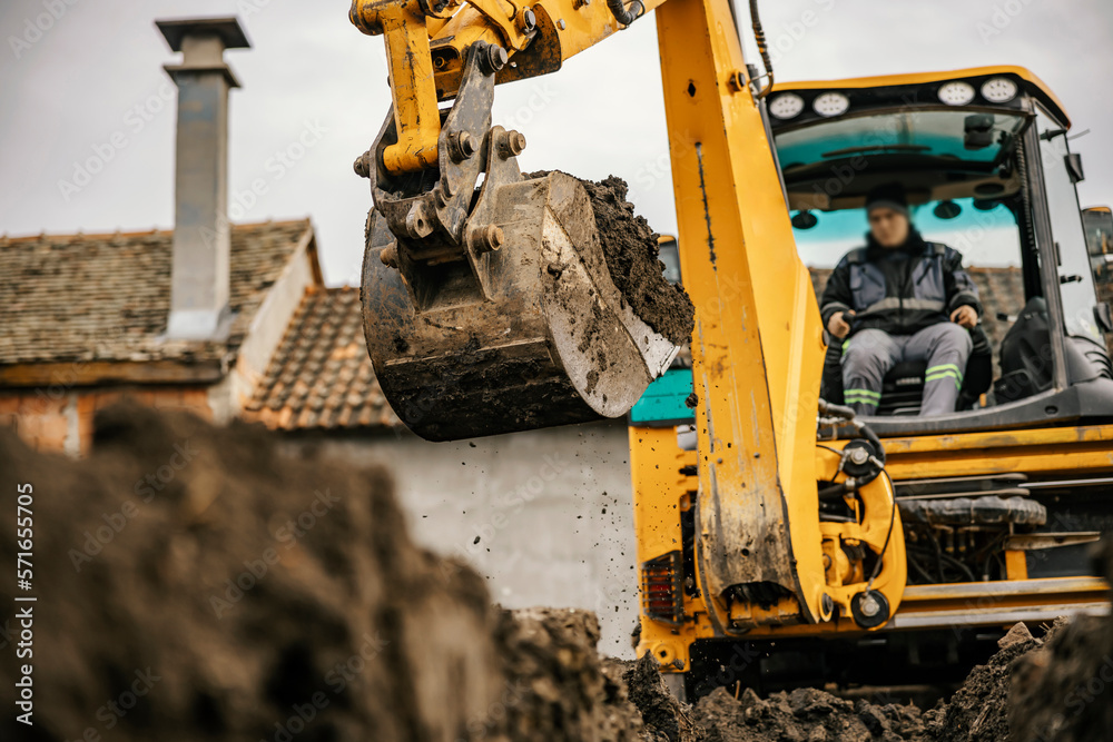 Fototapeta premium A worker in a backhoe is digging pit on a reconstruction area.