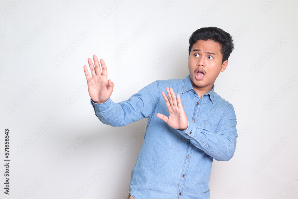 Portrait of scared Asian man in blue shirt forming a hand gesture to ...