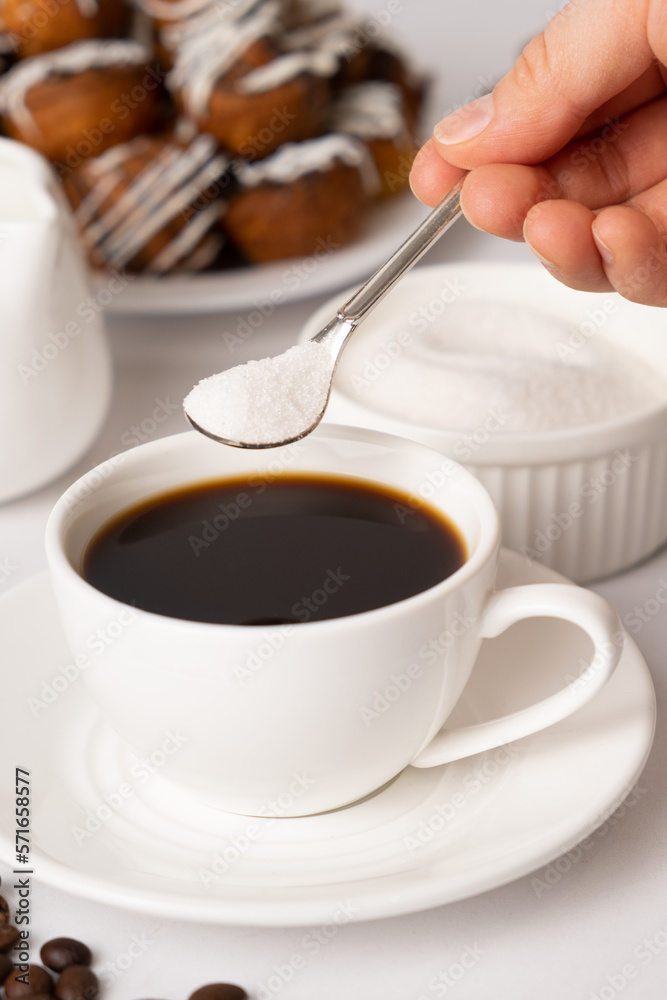 The process of pouring white sugar from a spoon into a white cup of coffee. Sugar addict, diabetes. The process of pouring white sugar from a spoon into a white cup of coffee. Sugar addict, diabetes.