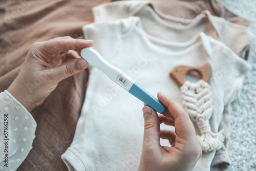 Positive pregnancy test on the background of cute baby clothes