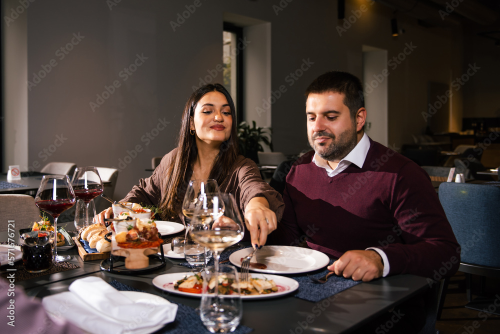 Group of joyful young man and woman having fun, passing and sharing food across table