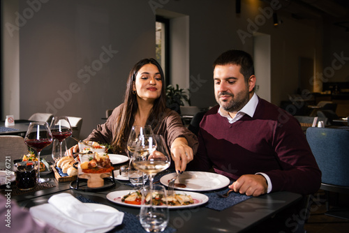 Group of joyful young man and woman having fun, passing and sharing food across table