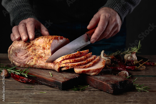 Hands of a male butcher cutting spicy ham.