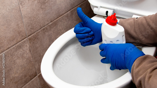 The cleaning lady near the toilet with cleaning agent shows the ok sign with her hand. The toilet is clean