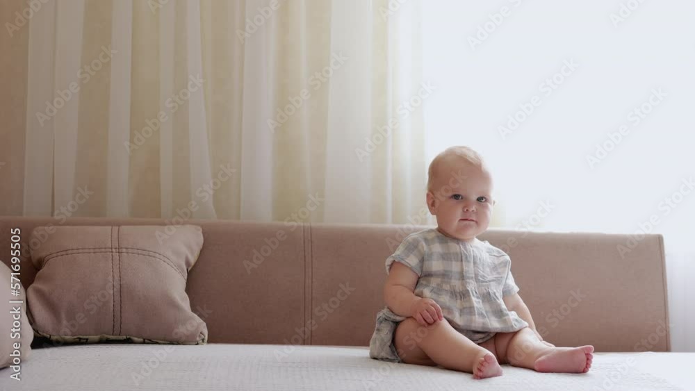 Adorable caucasian baby girl with different emotions, serious and smiling sitting on beige sofa at living room. International Children day. Carefree healthy babyhood, healthcare and paediatrics care. Adorable caucasian baby girl with different emotions, serious and smiling sitting on beige sofa at living room. International Children day. Carefree healthy babyhood, healthcare and paediatrics care.