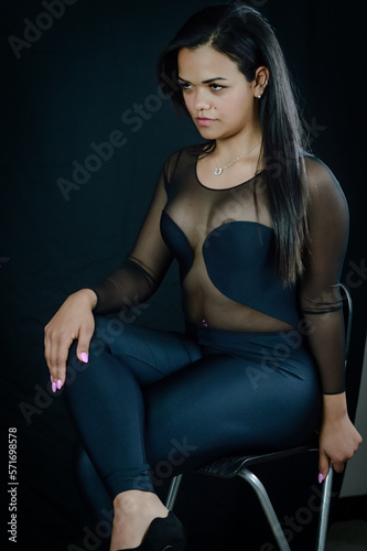 Portrait of a beautiful young Brazilian woman sitting on a stool and wearing a skintight body suit photo