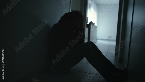 One anxious depressed woman covering face in despair sitting at home in the dark. Person suffering alone in corridor feeling shame and regret