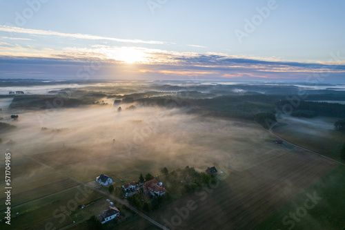 Foggy morning on a beautiful lake surrounded by forests and fields. A small village located near a lake in fog and morning sun.