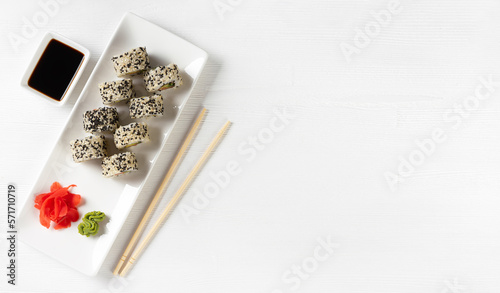Sushi roll California with salmon, sesame seeds, avocado, cream cheese on white background. Rolls served on white dish with wasabi, ginger and soy sauce. Japanese cuisine food. Top view, copy space
