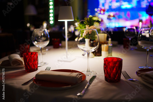 a table with a white tablecloth, glasses, crockery and decor in dark restaurant