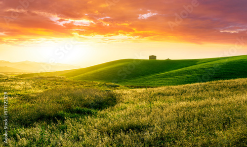 countryside sunset in green hills of spring fields with old castle farm and mountains on background of evening landscape