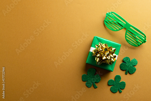 Image of green glasses, green clover, green present and copy space on orange background