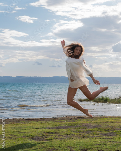 Smiling woman jumping mid air by the sea, Trevignano Romano, Lazio, Italy photo