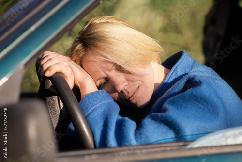 Tired woman driving a car. A middle-aged woman in her forties leaned over the steering wheel of a car. Fatigue, exhaustion, rest during the trip.