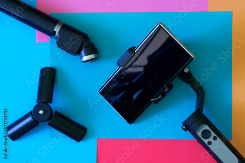 Mobile phone - smartphone mounted on selfie stick – stabilizer, gimbal for photo-video shooting and small tripod. Gadgets for blogging, streaming and video conferencing. Colored background. photo