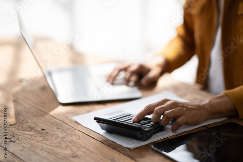 Close up view of man hand using calculator while typing on laptop computer.