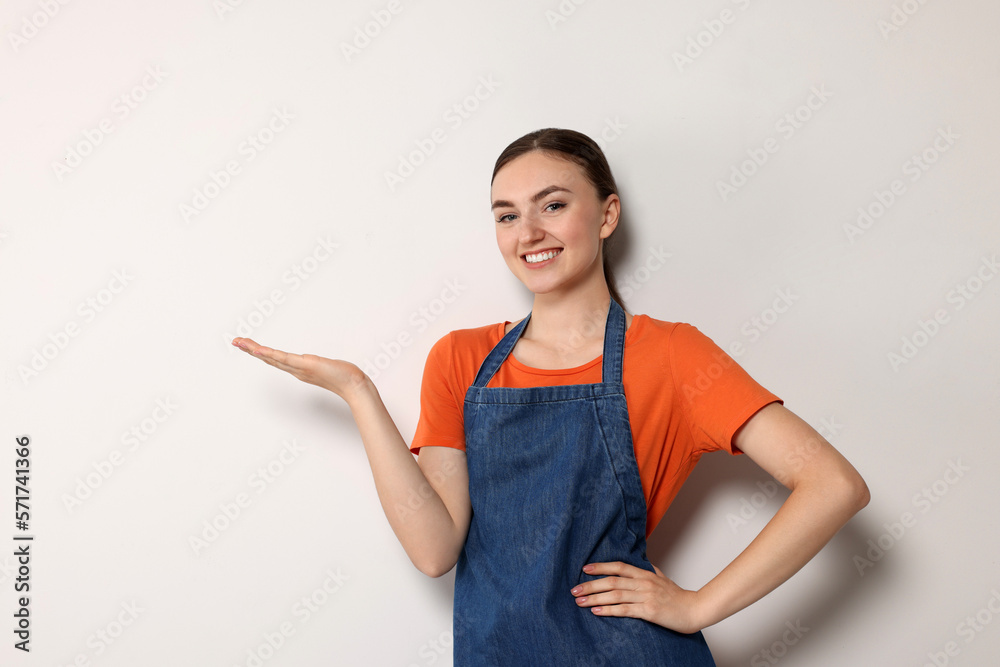 Beautiful young woman in clean denim apron on light grey background. Space for text Beautiful young woman in clean denim apron on light grey background. Space for text