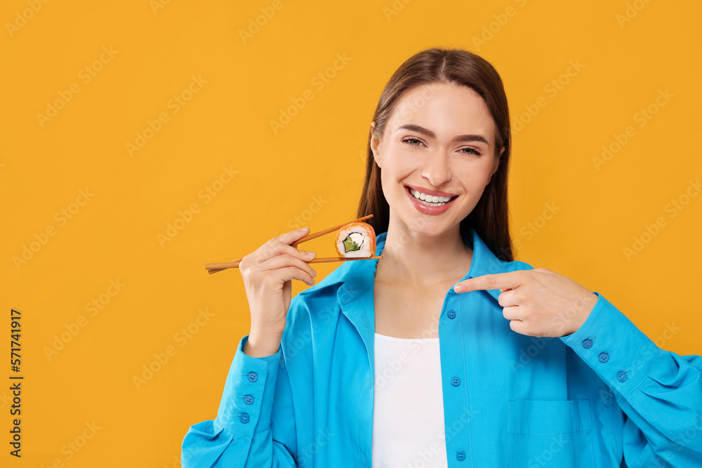 Happy beautiful young woman holding sushi roll with chopsticks on orange background. Space for text Happy beautiful young woman holding sushi roll with chopsticks on orange background. Space for text